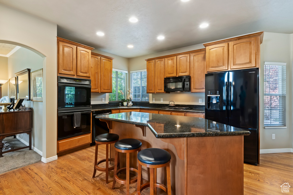 Kitchen with black appliances, a kitchen island, light wood finished floors, a breakfast bar, and recessed lighting