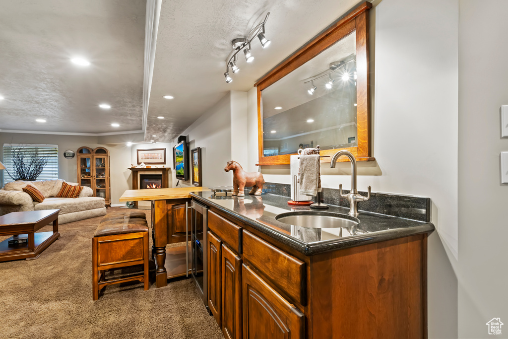 Indoor wet bar with recessed lighting, dark colored carpet, a warm lit fireplace, beverage cooler, and crown molding