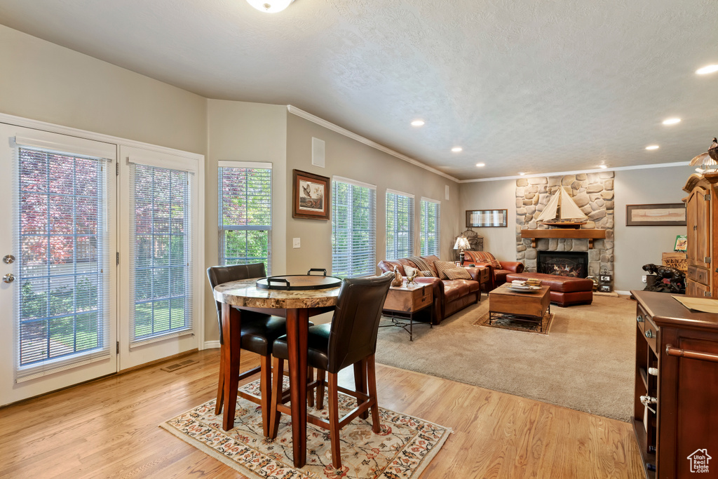 Dining space with ornamental molding, a stone fireplace, light wood-style floors, recessed lighting, and a textured ceiling