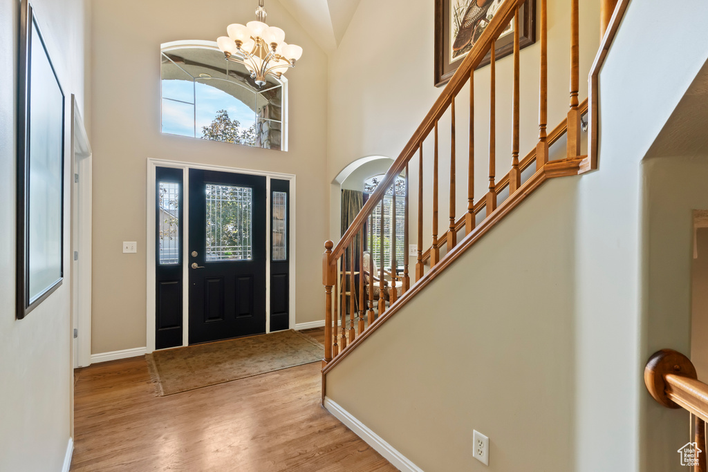 Foyer entrance featuring wood finished floors, a chandelier, baseboards, stairway, and a towering ceiling