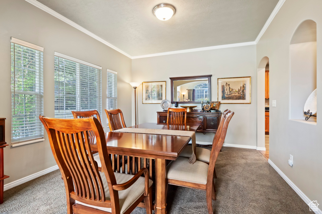 Carpeted dining area with arched walkways, plenty of natural light, crown molding, and baseboards