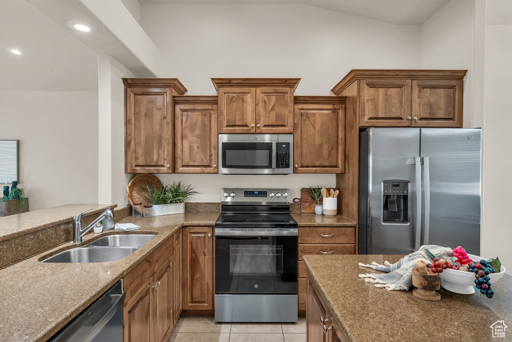 Kitchen with stainless steel appliances, a sink, dark stone countertops, brown cabinets, and recessed lighting