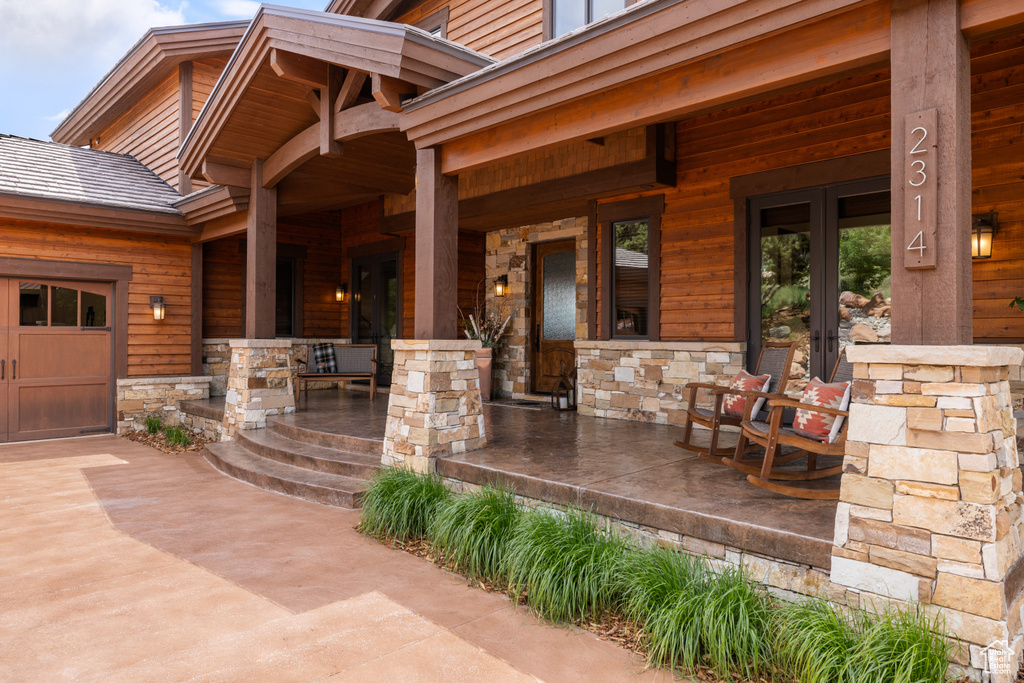 Covered porch featuring french doors, an attached garage, and driveway