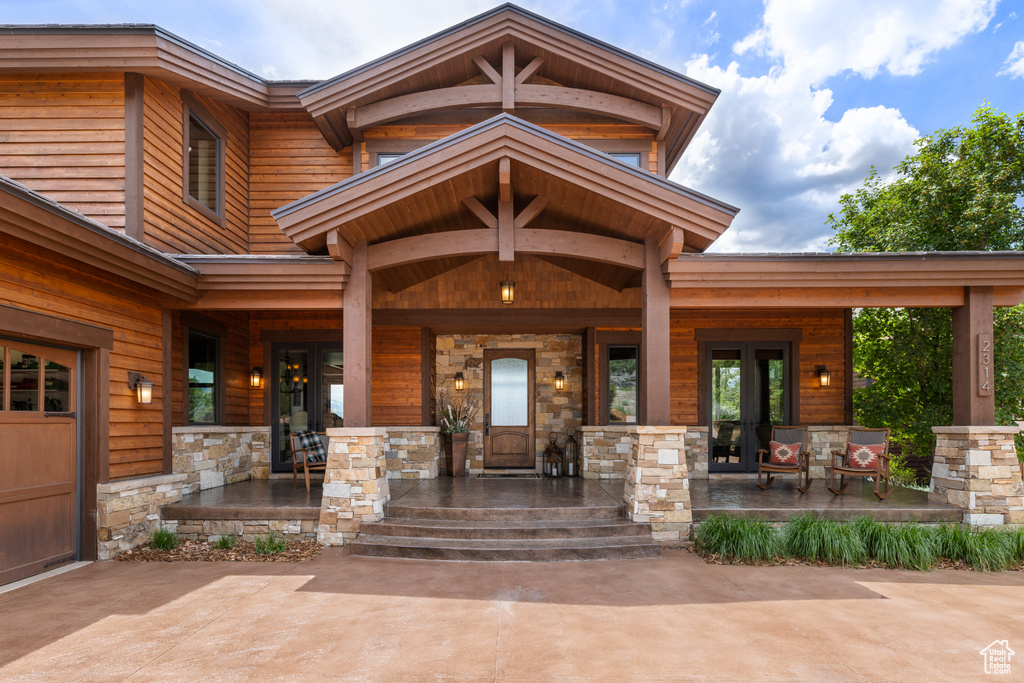 View of exterior entry featuring covered porch, stone siding, and french doors