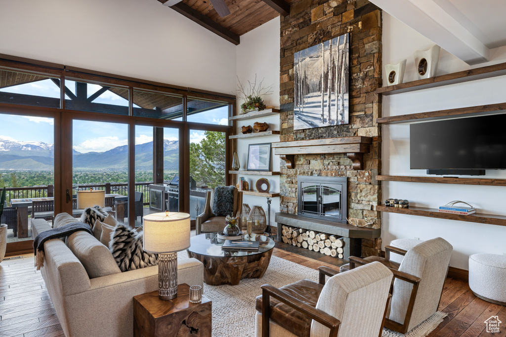 Living room featuring wood-type flooring, wood ceiling with exposed beams, a mountain view, a stone fireplace, and plenty of natural light