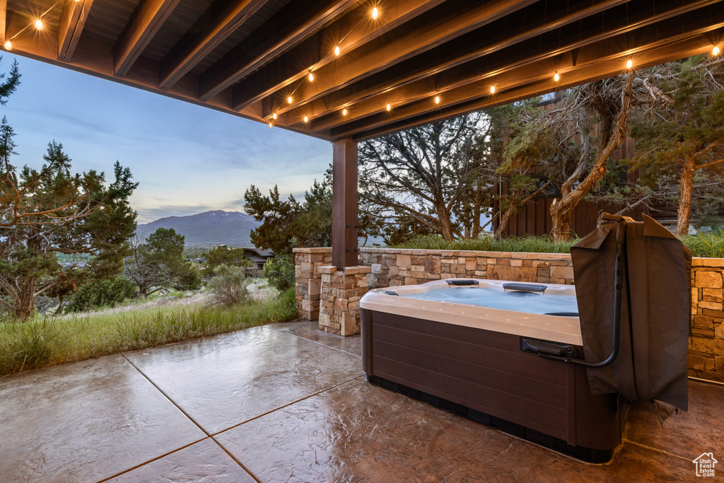 Patio terrace at dusk with a hot tub, a patio area, and a mountain view