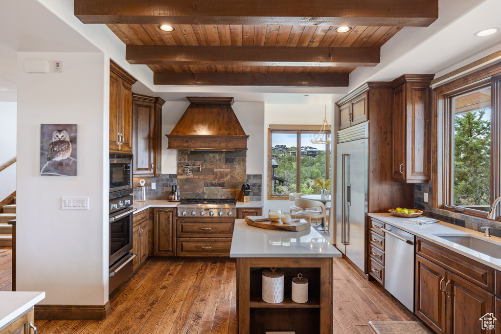 Kitchen with built in appliances, custom exhaust hood, wooden ceiling with exposed beams, plenty of natural light, and light countertops