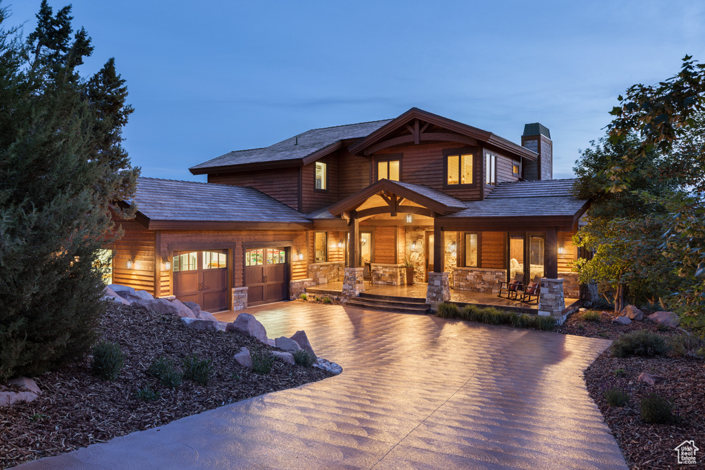 View of front of home with a porch, concrete driveway, a chimney, an attached garage, and stone siding