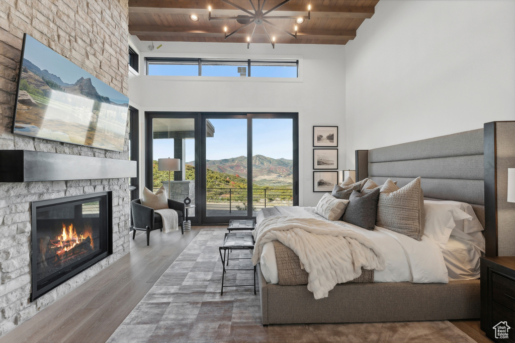 Bedroom with wooden ceiling with exposed beams, access to exterior, a stone fireplace, wood finished floors, and a mountain view