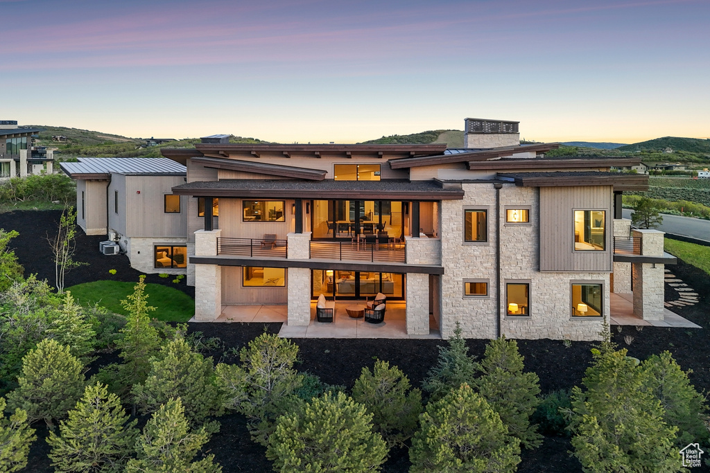 Back of property at dusk with a balcony, a patio, and stone siding