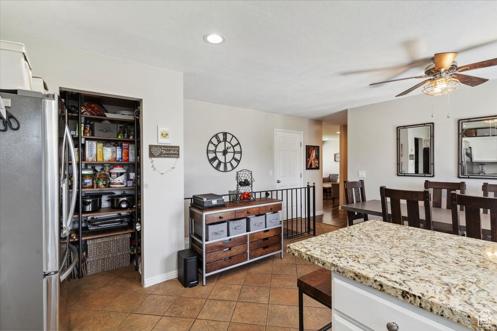 Kitchen featuring freestanding refrigerator, ceiling fan, tile patterned floors, light stone counters, and a kitchen bar