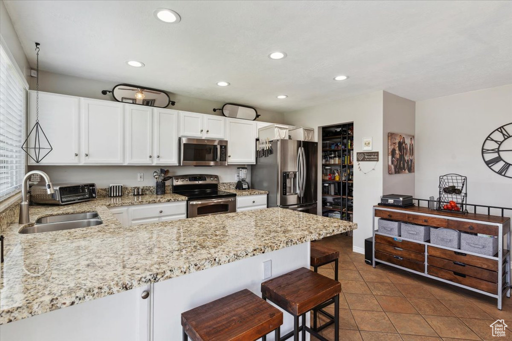Kitchen with appliances with stainless steel finishes, a sink, a peninsula, white cabinetry, and light stone counters