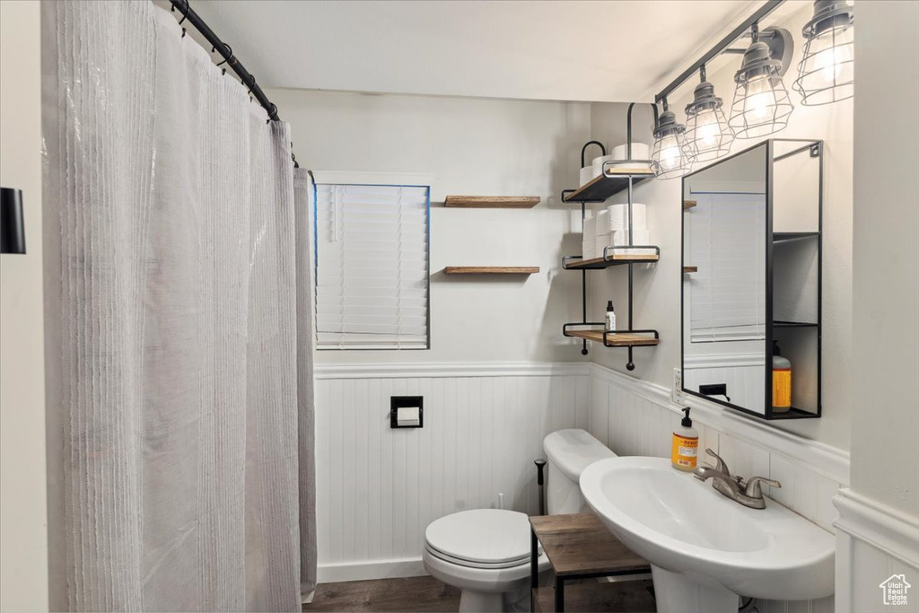 Bathroom featuring wainscoting, toilet, a sink, wood finished floors, and a shower with shower curtain