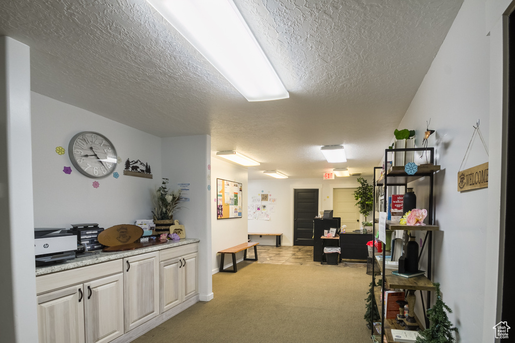 Hall with a textured ceiling, a desk, light colored carpet, and baseboards