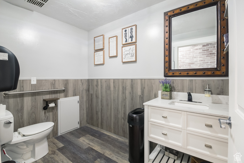 Half bathroom with toilet, a wainscoted wall, wood finished floors, and vanity