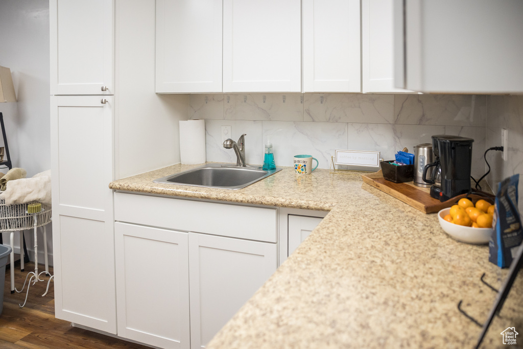 Kitchen featuring a sink, white cabinets, tasteful backsplash, dark wood-type flooring, and light stone counters