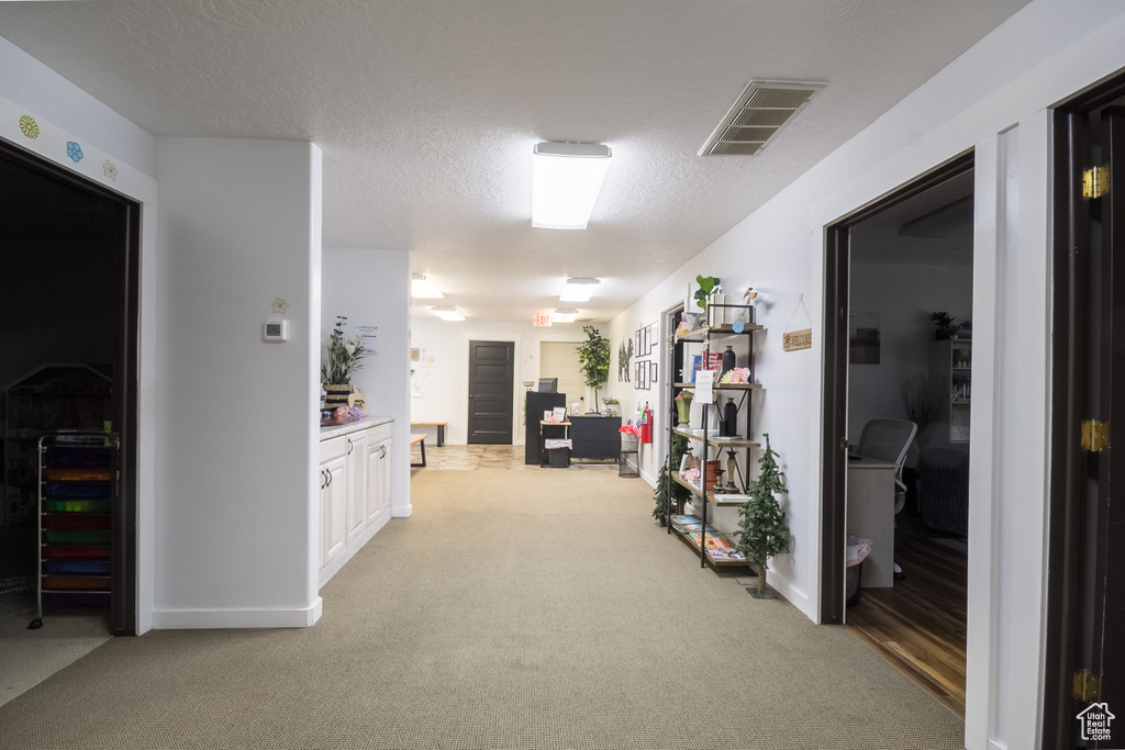 Corridor featuring light carpet, a desk, baseboards, and a textured ceiling