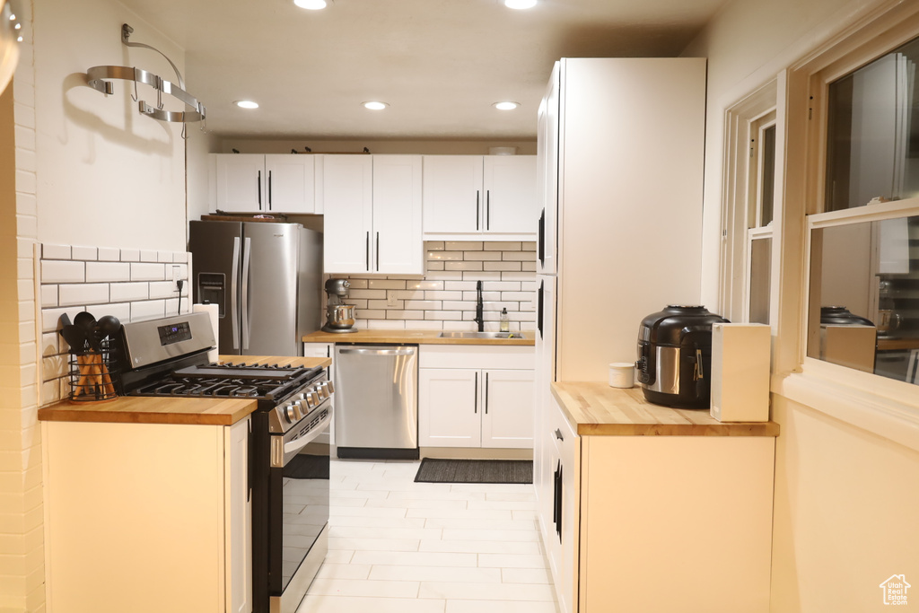 Kitchen featuring wooden counters, appliances with stainless steel finishes, recessed lighting, a sink, and white cabinets