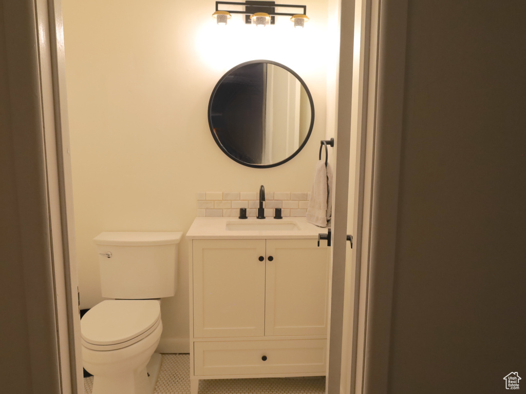 Half bath with vanity, toilet, tile patterned floors, and tasteful backsplash