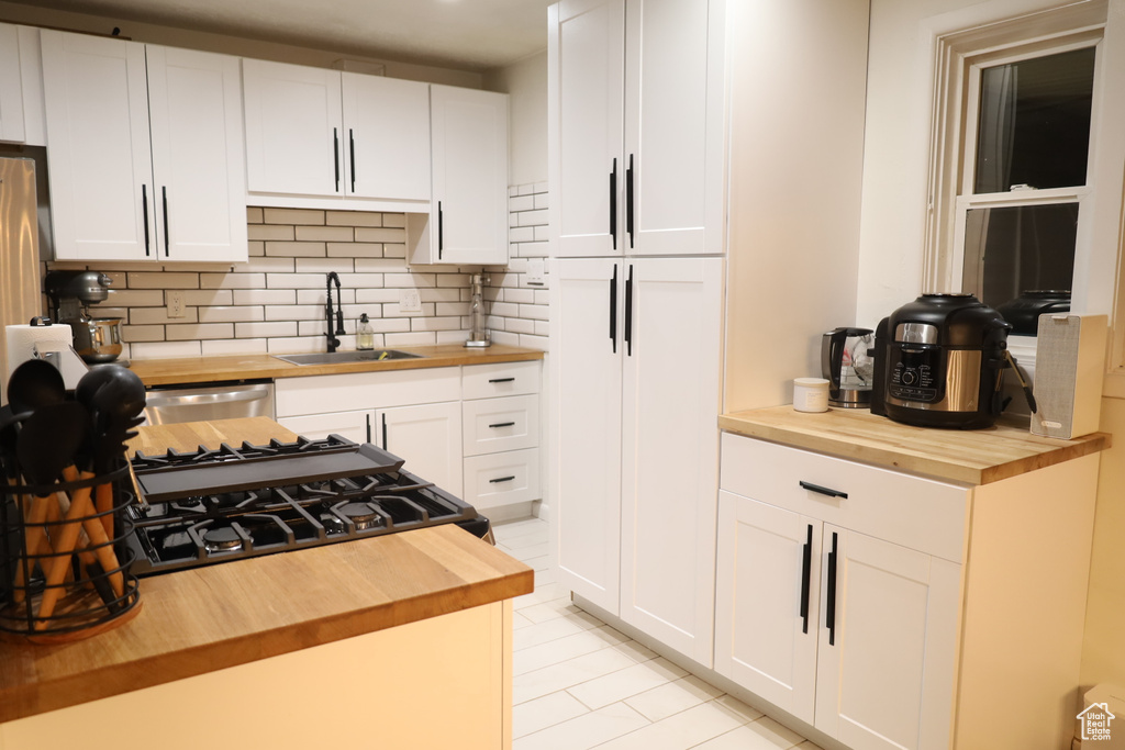 Kitchen with butcher block countertops, a sink, backsplash, white cabinets, and light tile patterned flooring