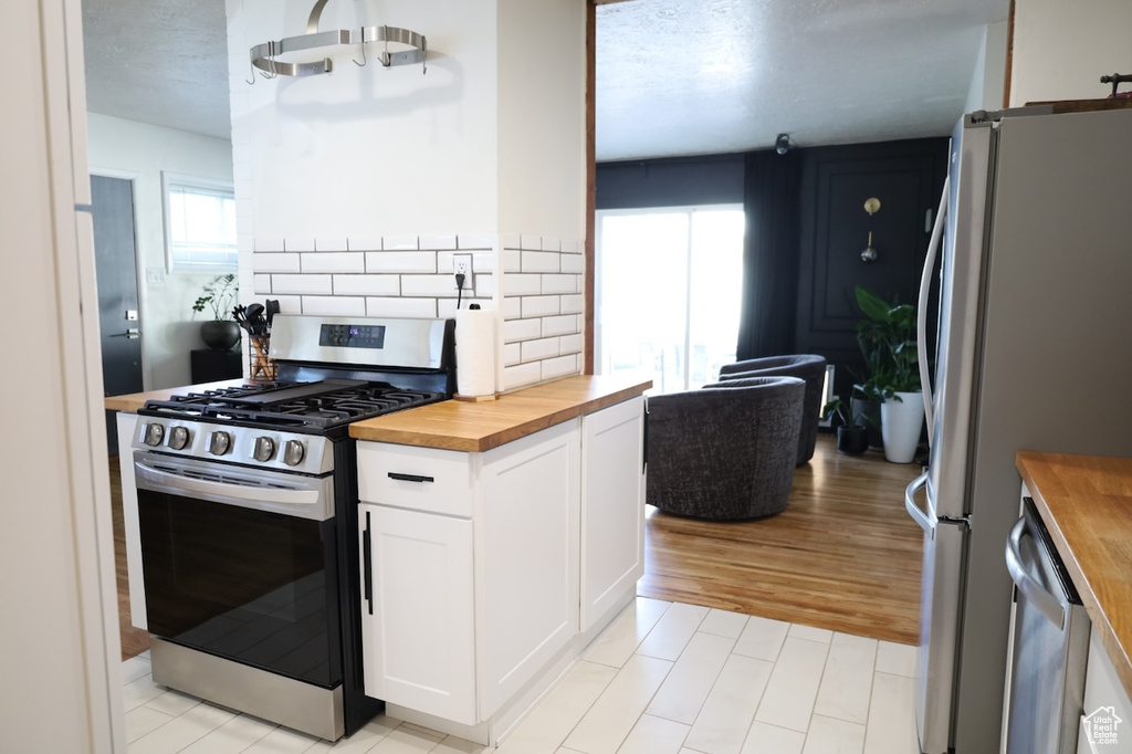 Kitchen featuring wooden counters, appliances with stainless steel finishes, white cabinetry, tasteful backsplash, and light wood finished floors