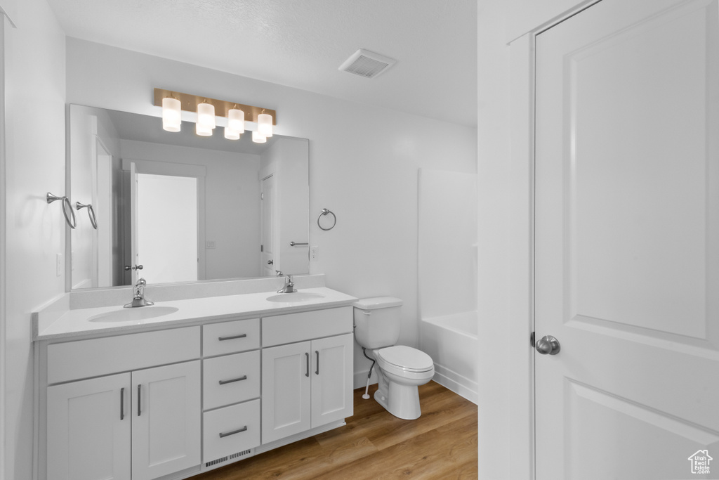 Bathroom with double vanity, toilet, and wood finished floors