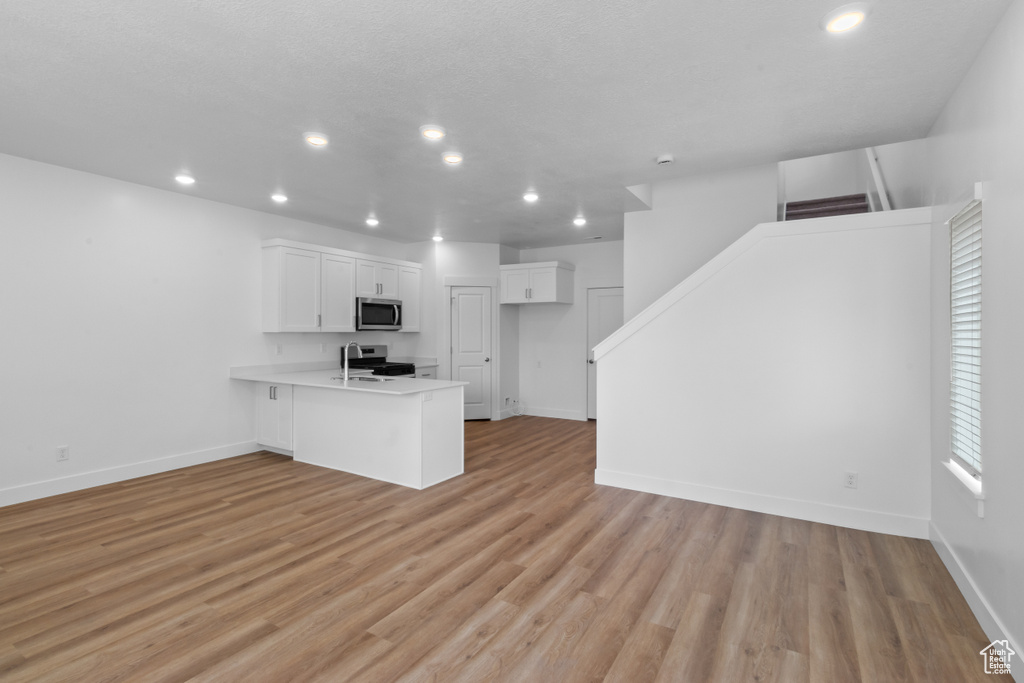 Kitchen featuring stainless steel microwave, a peninsula, recessed lighting, white cabinetry, and a sink