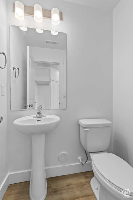 Half bath with baseboards, toilet, and wood finished floors