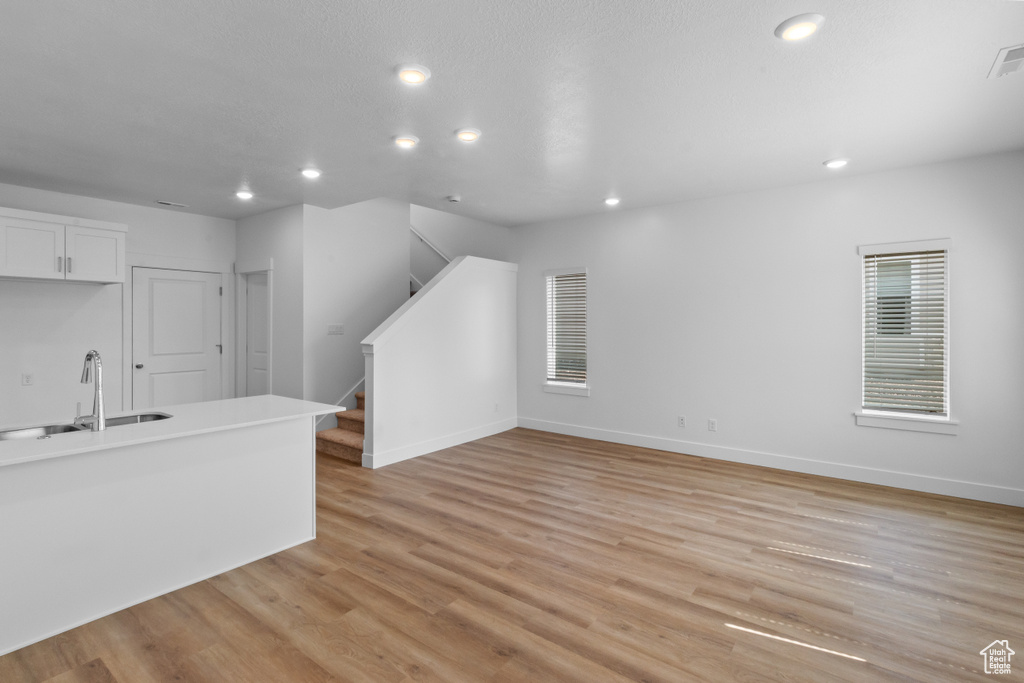 Unfurnished living room featuring a sink, recessed lighting, stairs, light wood finished floors, and baseboards
