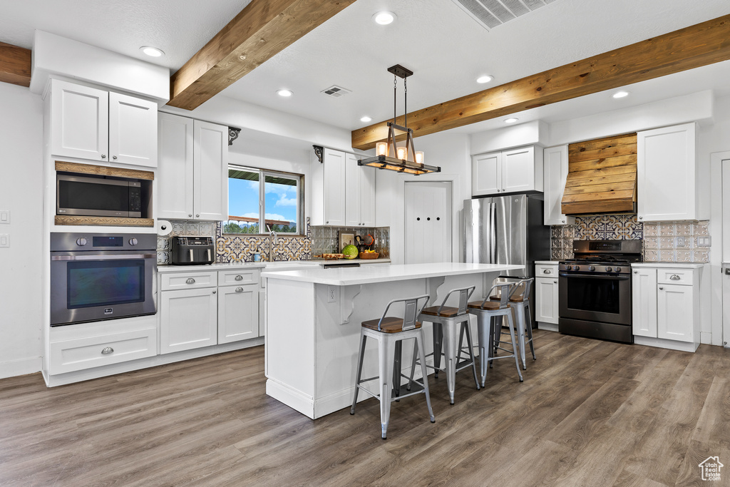 Kitchen featuring stainless steel appliances, beam ceiling, recessed lighting, wood finished floors, and white cabinets