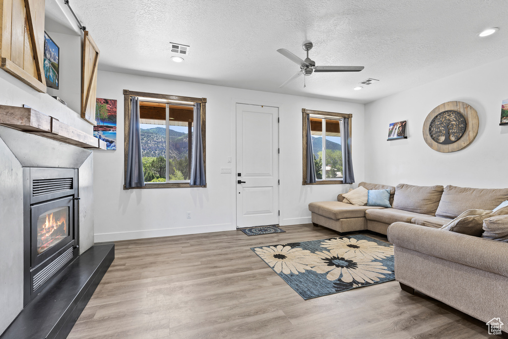 Living area featuring a glass covered fireplace, plenty of natural light, a textured ceiling, ceiling fan, and wood finished floors