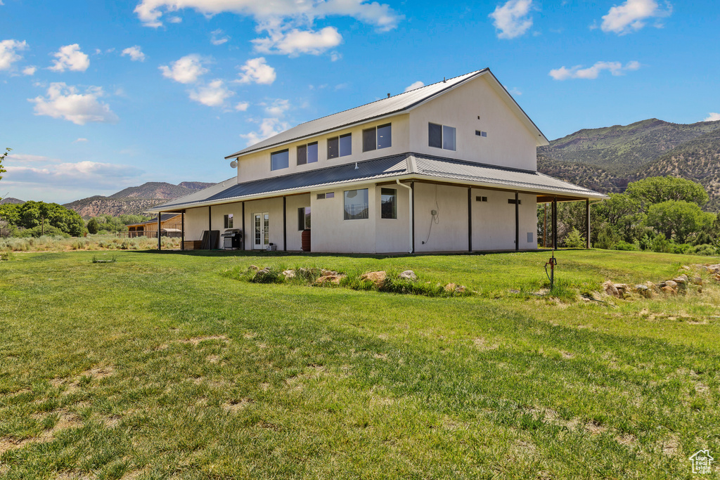 Back of house with a mountain view, a lawn, and metal roof