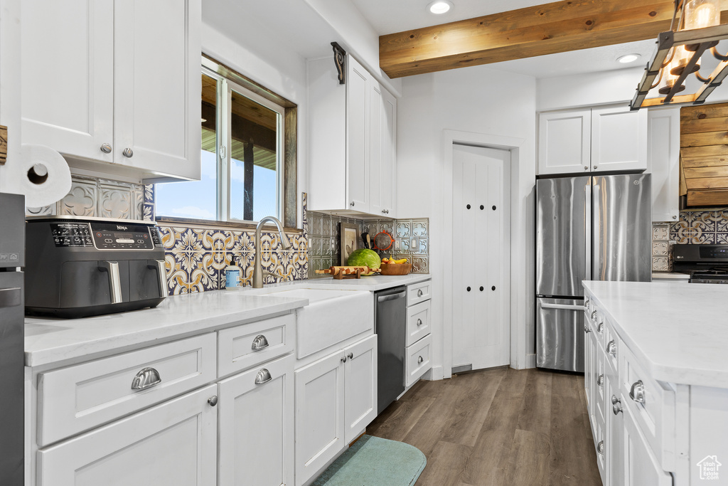 Kitchen featuring stainless steel appliances, backsplash, white cabinets, beamed ceiling, and a sink