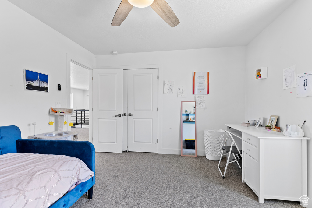 Carpeted bedroom with an office area, ceiling fan, and a closet