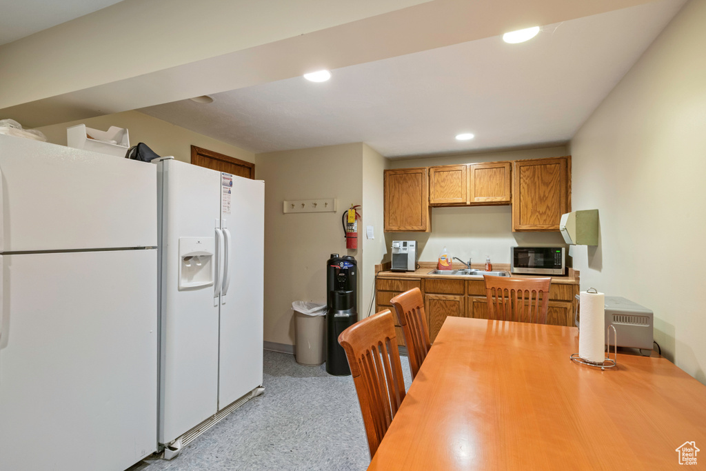 Kitchen with white refrigerator with ice dispenser, stainless steel microwave, a sink, light countertops, and recessed lighting