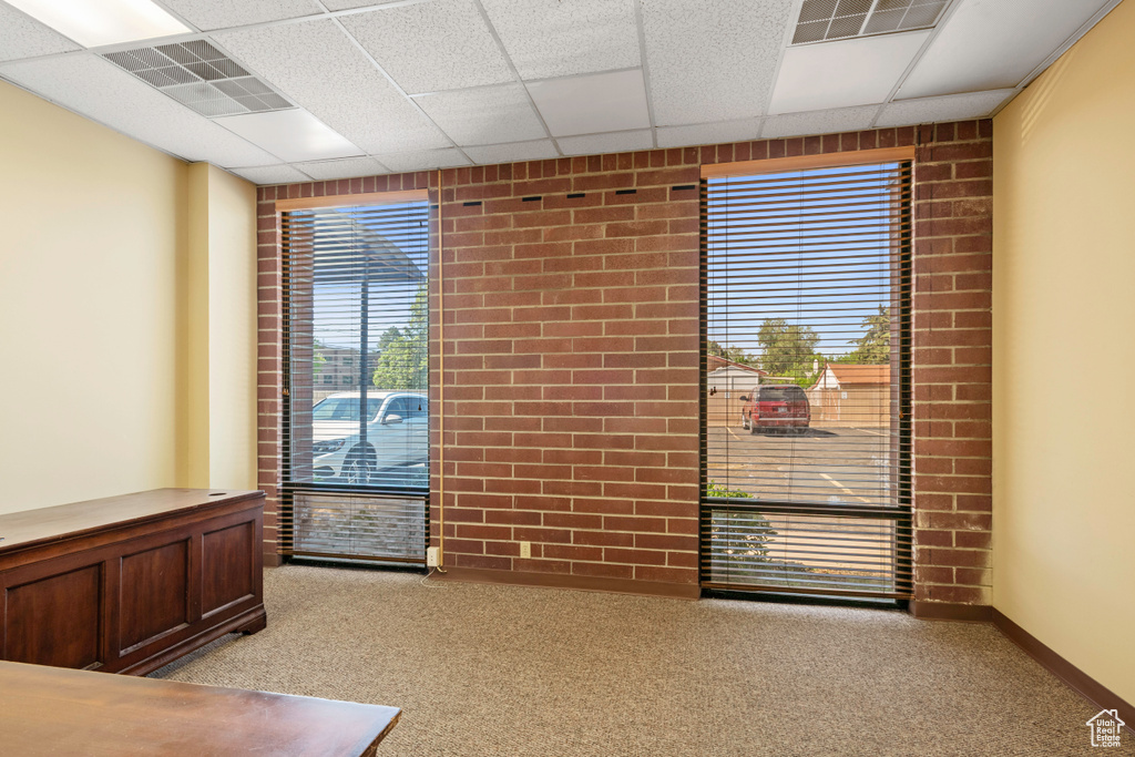 Spare room with light carpet, a paneled ceiling, and brick wall