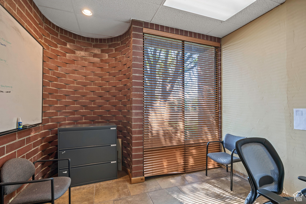 Office space with a paneled ceiling and brick wall