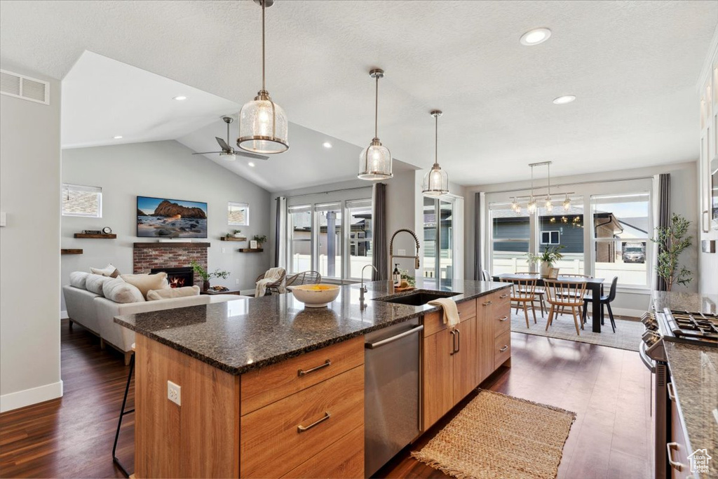 Kitchen with stainless steel appliances, a sink, dark wood-style flooring, a kitchen island with sink, and baseboards