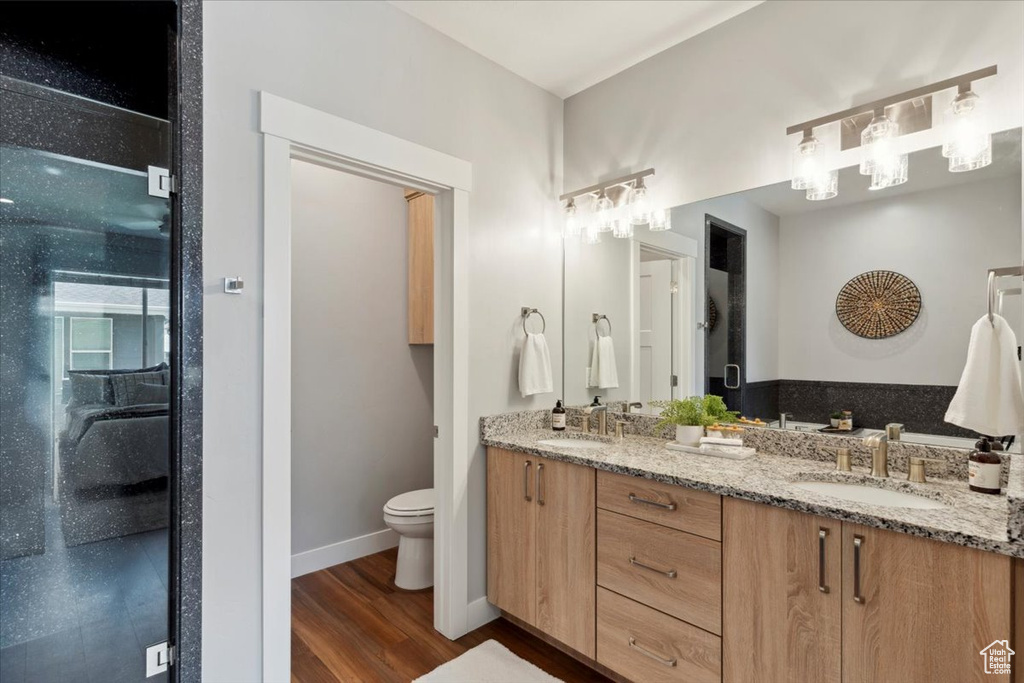 Full bath with double vanity, wood finished floors, toilet, and baseboards