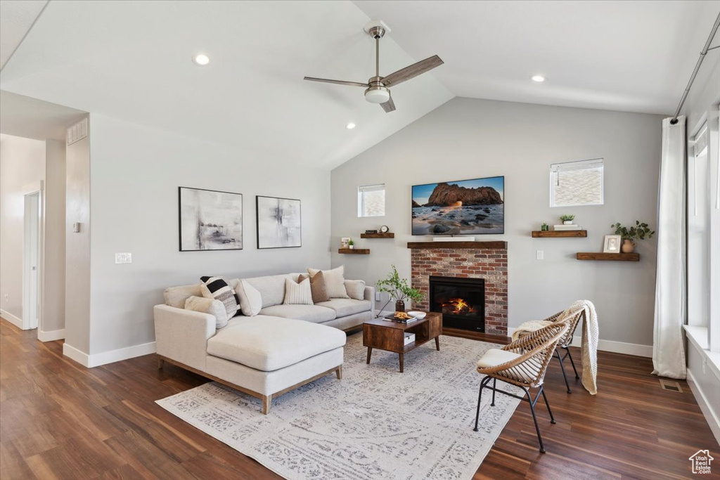 Living room featuring baseboards, dark wood-style floors, vaulted ceiling, a fireplace, and ceiling fan