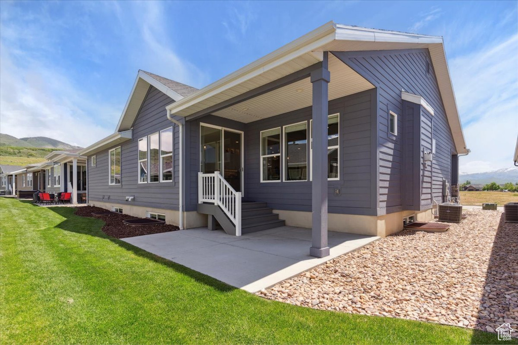 View of front of home featuring a mountain view, a patio, a front yard, and central AC