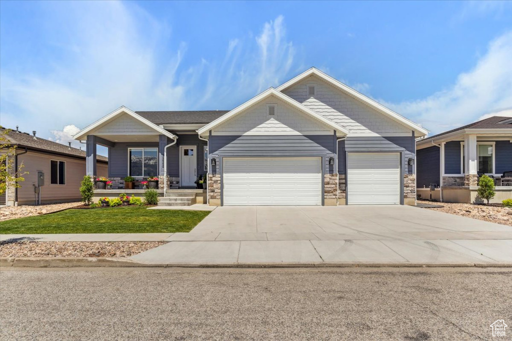 Craftsman house featuring a garage, a porch, a front yard, driveway, and stone siding