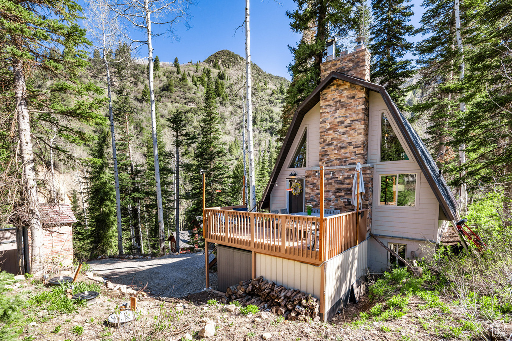 Back of property featuring a chimney, a deck with mountain view, and a wooded view