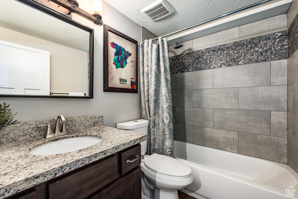 Full bath featuring toilet, vanity, shower / bath combo, and a textured ceiling