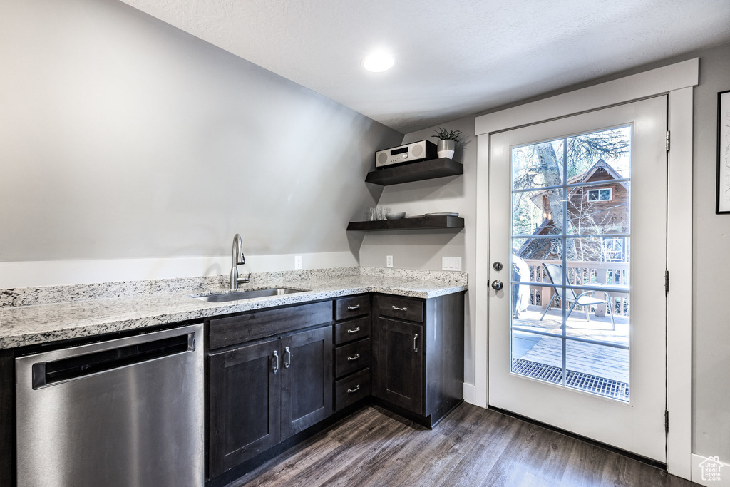 Kitchen with stainless steel dishwasher, a sink, open shelves, dark wood finished floors, and light stone countertops