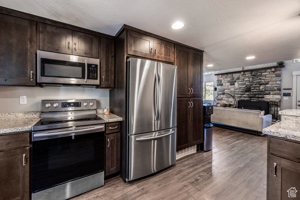 Kitchen with appliances with stainless steel finishes, open floor plan, dark brown cabinetry, wood finished floors, and a textured ceiling