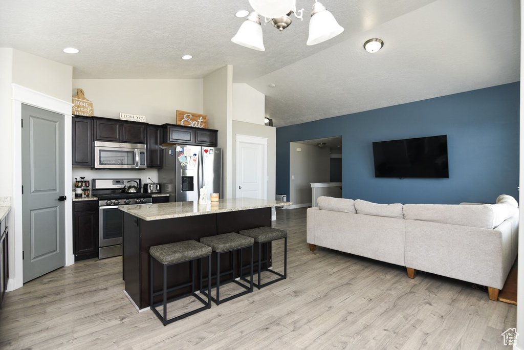 Kitchen featuring appliances with stainless steel finishes, a kitchen island, a breakfast bar, high vaulted ceiling, and light stone counters