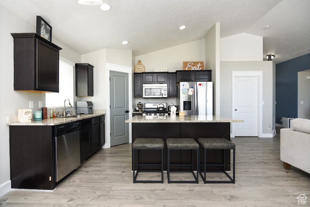 Kitchen with stainless steel appliances, a sink, lofted ceiling, light stone counters, and a kitchen bar