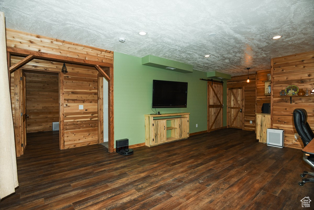 Unfurnished living room featuring a barn door, wood finished floors, recessed lighting, baseboards, and wooden walls