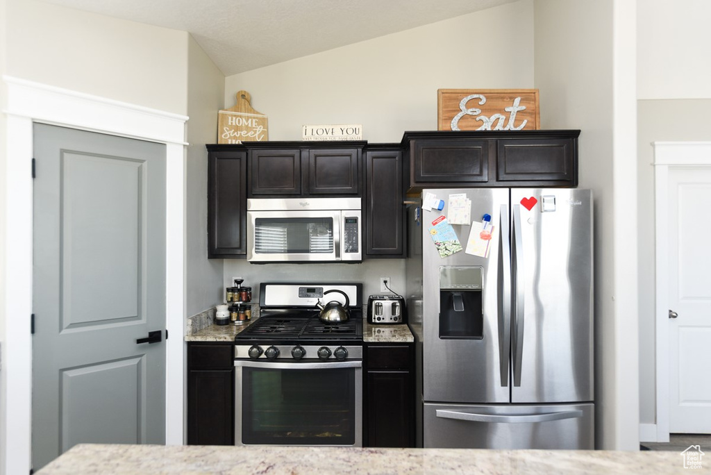 Kitchen with stainless steel appliances, vaulted ceiling, and light stone countertops